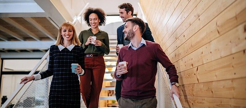 four happy colleagues walking downstairs with coffees