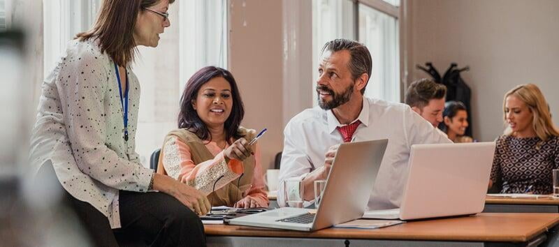 three colleagues sitting around laptops and talking